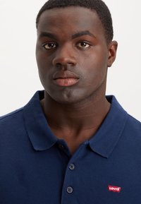 Polo azul-marinho feito de algodão com tecido texturizado, apresentando uma pala de dois botões e um logótipo vermelho da Levi's no peito.