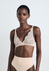 Bralette de renda em tom nude com uma delicada borda em scallop e alças largas, combinado com cuecas de cintura alta em tom nude, de textura suave.
