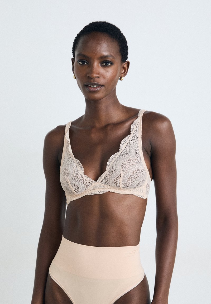 Bralette de renda em tom nude com uma delicada borda em scallop e alças largas, combinado com cuecas de cintura alta em tom nude, de textura suave.
