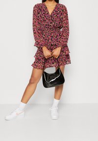 Blommig omlottklänning med långa ärmar, volangkant, svart bakgrund och rosa, gula blommönster. Matchad med en svart, glansig handväska och vita sneakers.