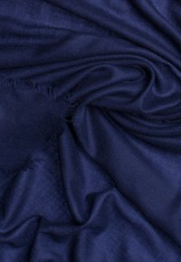 Tissu bleu marine à la texture lisse, présentant un tombé doux et des bords effilochés, affichant de subtiles variations de teinte et de lumière.