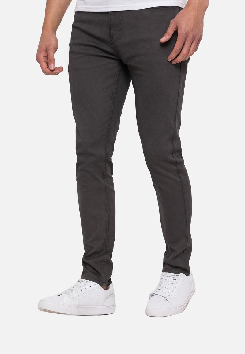 Tummanharmaat, kapealahkeiset farkut, jotka on valmistettu puuvillasekoitteesta. Farkuissa on tavalliset taskut ja hienovaraiset ompeludetaljit. Ne on yhdistetty valkoisiin tennareihin.