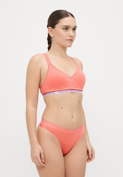 Coral athletic lingerie set featuring a soft, stretchy fabric. The bra has a v-neck design with a logo band and matching low-rise underwear.