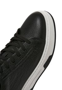 Sneaker in pelle nera con finitura texture, punta rotonda, lacci neri e suola in gomma bianca con un motivo di battistrada distintivo.