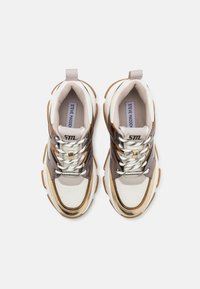 Des baskets avec un design en matériaux mélangés, présentant des accents blancs, marron et dorés. Semelle épaisse avec des lacets à motif et une languette.