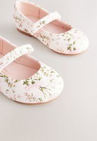 Chaussures Mary Jane blanches à motif floral avec un bout arrondi, une doublure rose et une bride réglable. Texture lisse en cuir synthétique, semelle plate.