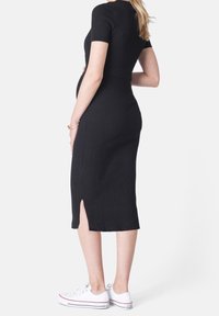 Musta ribattimidi-mekko lyhyillä hihoilla, jossa on sivureikä. Yhdistetty valkoisiin lenkkareihin, mikä korostaa rentoa tyyliä.