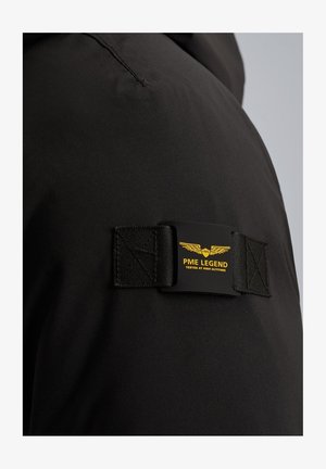 Zwarte waterdichte jas met een rechthoekige, merkgebonden patch met gele tekst en logo, vergezeld van gestructureerde zwarte banden.