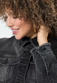 Mustat farkkutakki, jossa on risaiset hihansuut, nappisuljenta ja kauluskotelo, hieman haalistuneella pinnalla.