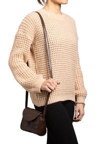 Maglione beige lavorato a maglia con un motivo testurizzato, polsini a costine e scollatura rotonda, abbinato a una borsa a tracolla in pelle marrone.