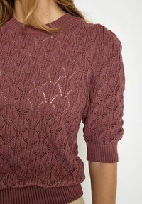 Roosa värviga kudum, millel on tekstuuriga lehepaisutus, lühikesed puhvikuued ja soonikuga alläär. Valmistatud kerge lõngaga.