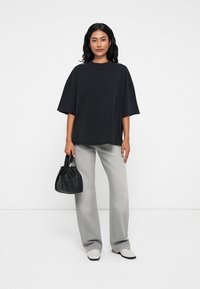 Μαύρη oversized μπλούζα με κοντά μανίκια, συνδυασμένη με ανοιχτό γκρι παντελόνι και μια μικρή μαύρη τσάντα. Παπούτσια είναι ανοιχτού χρώματος slip-ons.