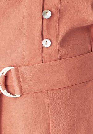 Roosade värvidega kangas, millel on vöö ümmarguse hõbedase kinnitusega ja kaks ümmargust nuppu läbipaistvast materjalist.