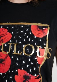 Camiseta negra con un gráfico audaz y letras doradas que dicen "Fabuloso", flores rojas sobre un fondo negro texturizado con acentos blancos.