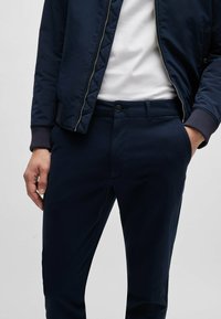 Marine bomberjack met een rits, gedragen over een wit T-shirt. Slim-fit marineblauwe pantalon met een knoopsluiting en zijzakken.