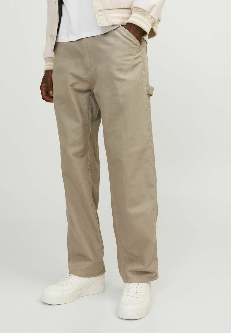 Pantalones cargo beige con detalles en los bolsillos laterales, hechos de una tela suave, con un corte relajado y acentos cosidos, combinados con zapatillas blancas.