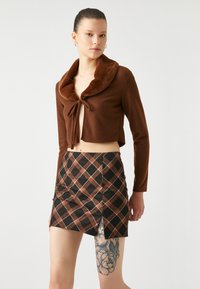 Bruine cropped trui met een nepbont kraag en een strik aan de voorkant, gecombineerd met een bruin, zwart en wit geruite minirok met een zijsplit.