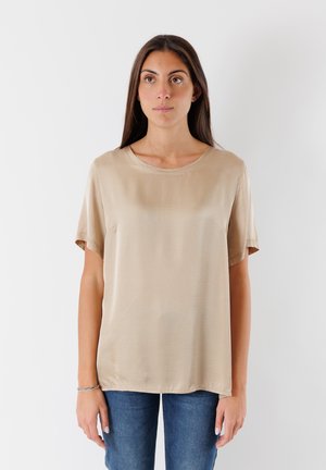 Top corto in seta beige con collo rotondo. Vestibilità rilassata e texture liscia, abbinato a jeans di denim blu.