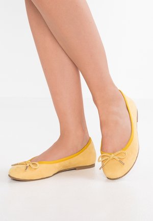 Żółte zamszowe baletki z cienkim żółtym wykończeniem i detalem kokardki na czubku. Niski profil z płaskim, zaokrąglonym czubkiem i minimalną ilością elementów metalowych.