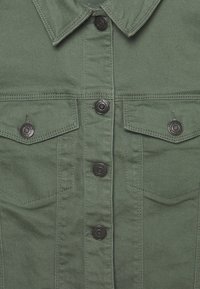 Chaqueta de denim verde con cuello afilado, botones a presión negros y dos bolsillos en el pecho con solapa. Tejido texturizado con costuras visibles.