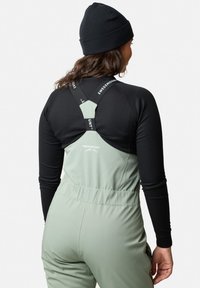 Grön skidoverall med svart långärmad tröja, med justerbara remmar, ribbat mönster och logotypdetalj på remmarna och ryggen.