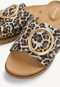 Open-toe slide sandals with tan footbeds, leopard print straps, and large round gold buckles.