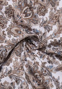 Tessuto con uno sfondo bianco caratterizzato da intricati motivi paisley marroni e blu. Texture liscia con motivi floreali sparsi.