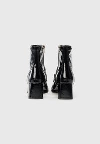 Sorte patentlær ankle boots med firkantet hæl, lynlås på siden og glat tekstur. Har en blank finish og kontureret design.