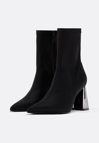 Črne gležnjarje iz raztegljivega materiala z ozkim nosom in debelim srebrnim peto. Gladka površina z minimalno vidnimi šivi.