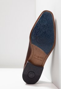 Semelle de chaussure habillée marron avec grip en caoutchouc texturé, marquage taille 42 et nom de marque "bugatti" embossé sur la partie en cuir.