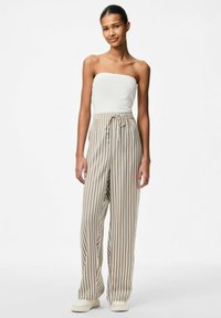 Witte geribbelde strapless top gecombineerd met beige gestreepte wijde pijpen broek met een elastische tailleband en trekkoord, gedragen met lichte schoenen.