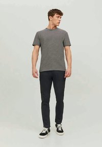 Man wearing black and white striped short-sleeve t-shirt, black pants, and black sneakers with white laces, looking right.