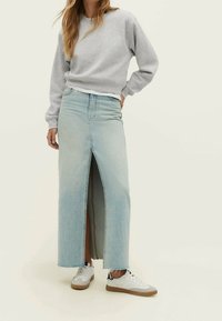 Jupe maxi en denim bleu clair avec fente à l'avant et ourlet effiloché, associée à un sweat-shirt gris et des baskets blanches. Design décontracté et coupe relax.