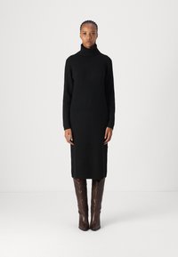 Črna rebrasta pletena obleka s turtleneck ovratnikom, do kolen, z dolgimi rokavi. V kombinaciji z rjavimi visokimi kavbojskimi čevlji z detajli.