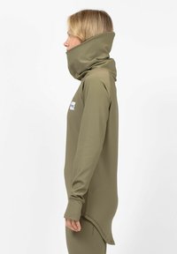 Olive green ribbed tunic with a high collar and elongated back hem, made from a smooth fabric. Features a small logo patch.