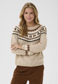 Pull en maille beige avec un empiècement à motifs dans des tons de marron, noir et blanc. Caractéristiques de manches longues avec des poignets décoratifs. Tissu texturé.