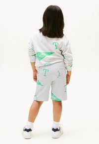 Grijze sweatshirt en shorts met groene logopatronen. De sweatshirt heeft een ronde hals; de shorts zijn knielang met een elastische tailleband.