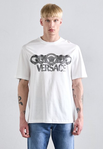 Weißes Baumwoll-T-Shirt mit einem Grafiken von einer silbernen Kette und einem runden Emblem mit dem Text "VERSACE" auf der Vorderseite. Kurze Ärmel, lockere Passform.