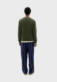 Suéter verde de manga larga, combinado con pantalones de tiro alto y pata de elefante a rayas en azul, marrón y detalles en crema.