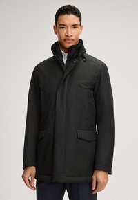 Schwarzer isolierter Mantel mit hohem Kragen, seitlichen Taschen und glatter Oberfläche. Verfügt über knöpfte Akzente und ein leichtes Design.