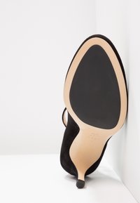 Chaussure à talon hauts en daim noir avec un bout pointu et une semelle nude lisse, dotée d'un talon mince et de détails de design minimalistes.