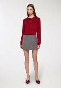 Czerwony dzianinowy polo z długim rękawem z trzema guzikami, zestawiony z szarą mini spódnicą z ukośnym przednim klapkiem i przednią kieszenią.