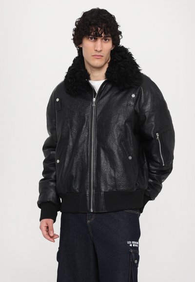 Zwarte leren bomberjack met een donzige zwarte kraag, gestructureerd oppervlak, ritssluitingen aan de zijkanten en geribbelde rand en manchetten.