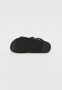 Svart sandal med en formad halkfri sula, utrustad med justerbara remmar. Botten har en ribbad textur för fäste och grepp.