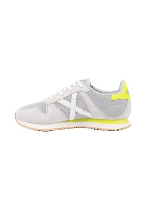 Zapatilla deportiva de malla en gris claro y blanco con cordones blancos, suela marrón clara y detalles en amarillo neón en el talón y la entresuela.