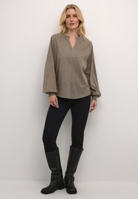 Olive zelená blůza s dlouhým rukávem, V výstřihem, textured puntíkovaným vzorem a nařasenými manžetami rukávů. S kombinací s černými skinny džínami a vysokými kozačkami.