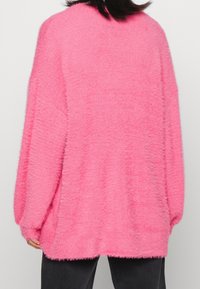 Fuzzy pink oversized sweater with a relaxed fit, featuring dropped shoulders and ribbed cuffs, made from soft, textured material.