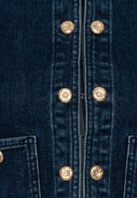 Tissu en denim bleu foncé avec des boutons dorés texturés disposés en deux rangées verticales autour d'une fermeture éclair centrale.