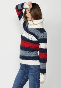 Pull rayé présentant des couleurs marine, gris, rouge et blanc, avec un col montant et des poignets côtelés, fabriqué en matériau tricoté doux.