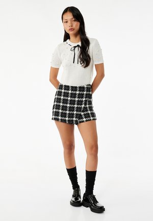 Haut tricoté blanc à manches courtes, décoré d'accents texturés, associé à une mini-jupe à carreaux noir et blanc, des chaussettes jusqu'à la cheville et des chaussures noires.